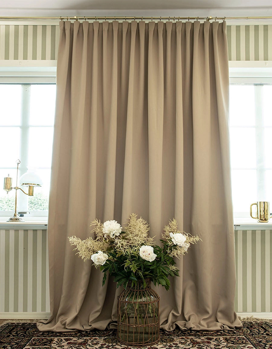 Beige gardin med fingerkrokar upphängd i gardinstång