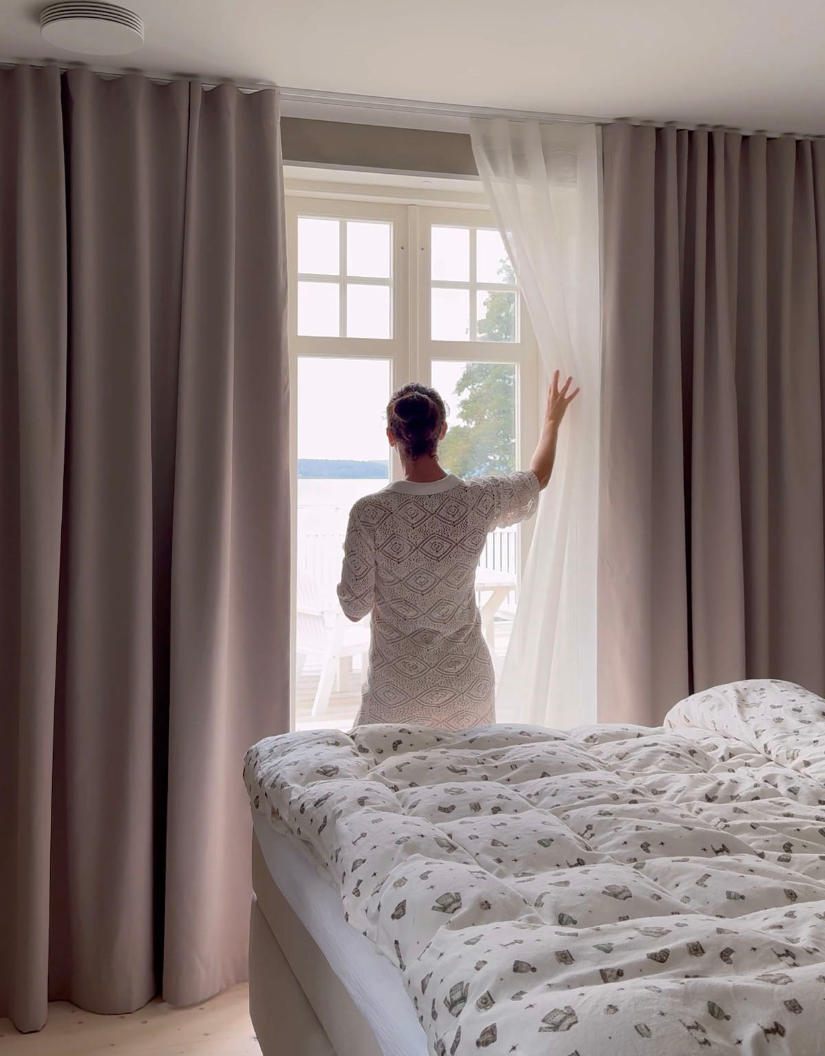 Kvinna som drar i gardiner i sovrum