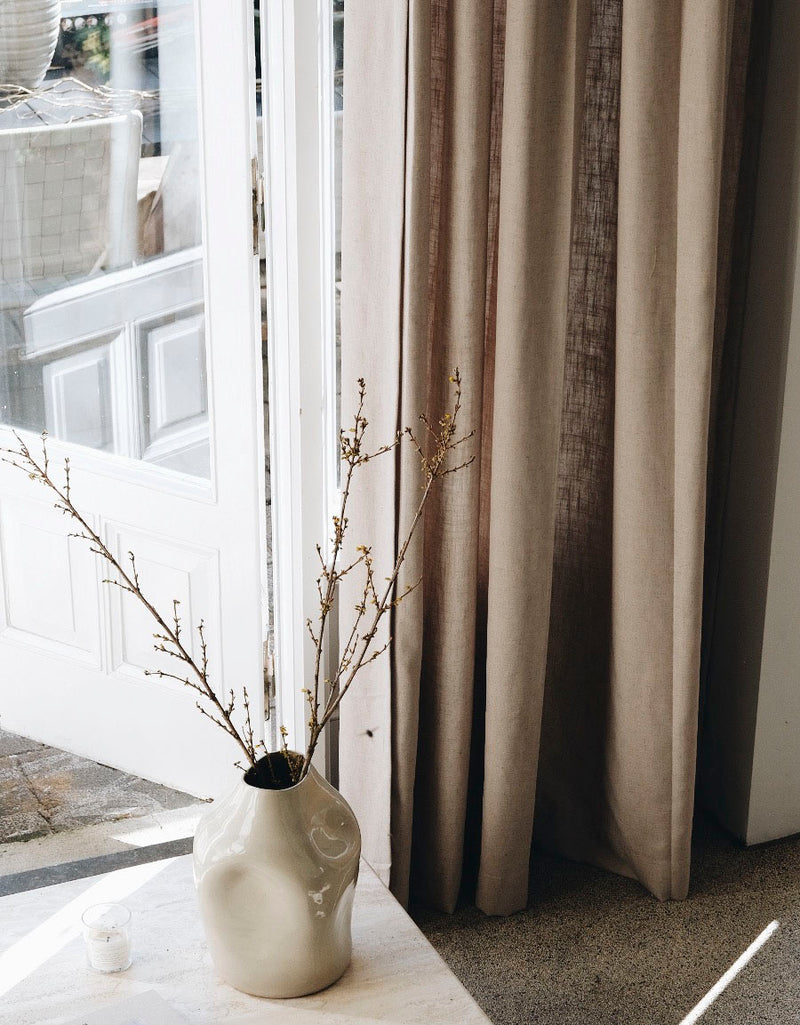 Beige linnegardin med en stor vas framför